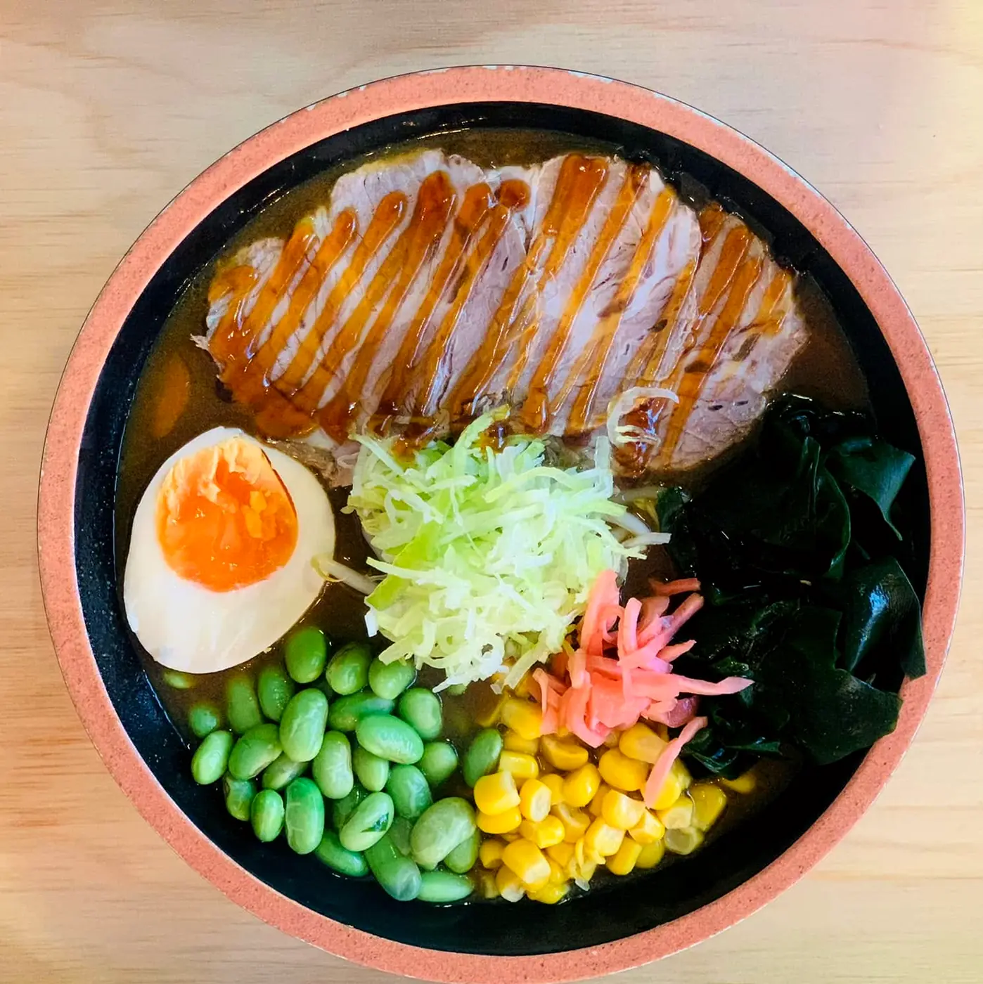 Miska ramenu z góry: chashu, połówka jajka nitamago, por, wakame, beni shoga, kukurydza, edamame w bulionie
